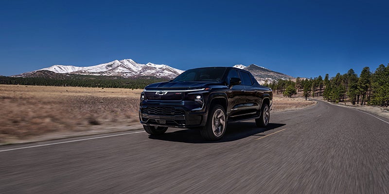 Black pickup truck driving on a paved road through an open landscape, shown from a front-left angle