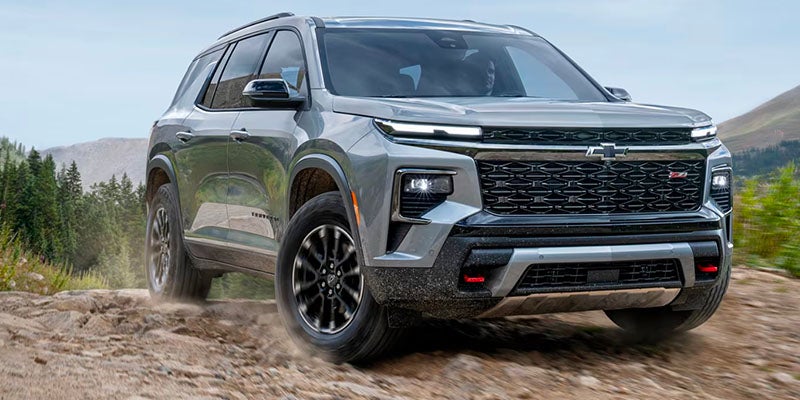 Gray Chevrolet SUV driving on a rocky dirt trail, kicking up dust, shown from a front-left angle