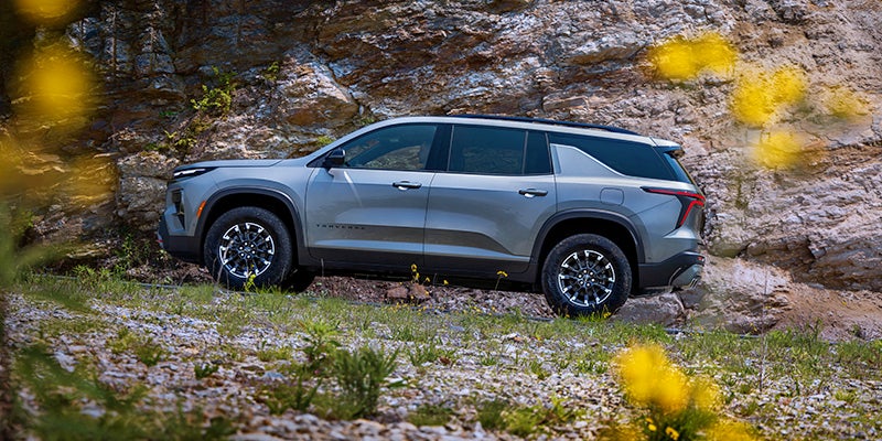 Gray midsize SUV parked on a rocky, grassy slope beside a cliff face, shown in side view
